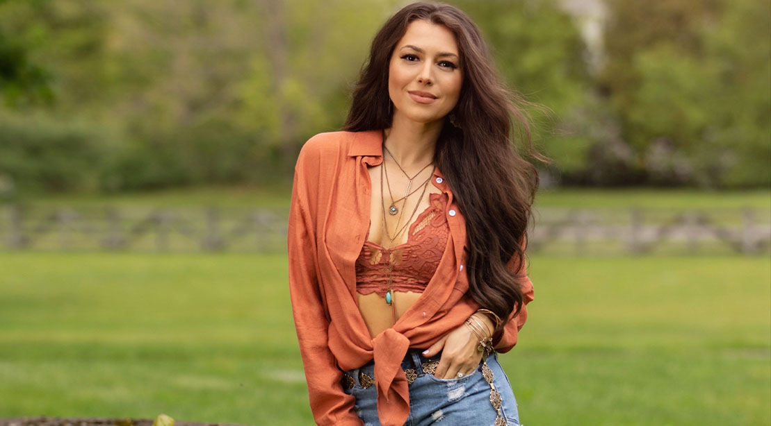 Country music star Jessica Lynn wearing a red blouse in a field