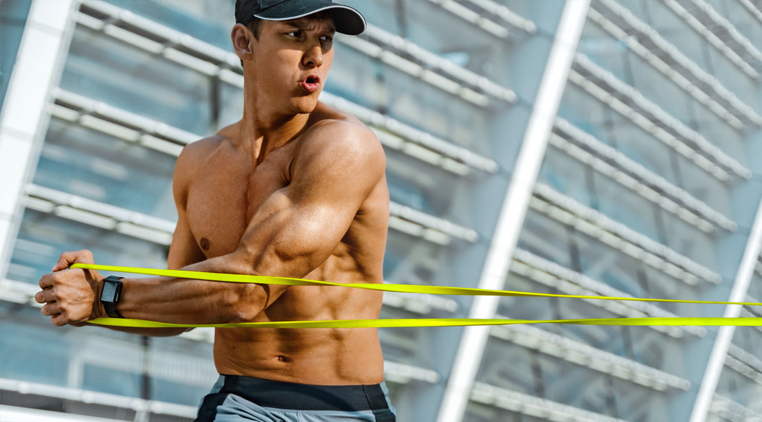 Muscular fit man performing a bodyweight band workout with a banded should rotations exercises