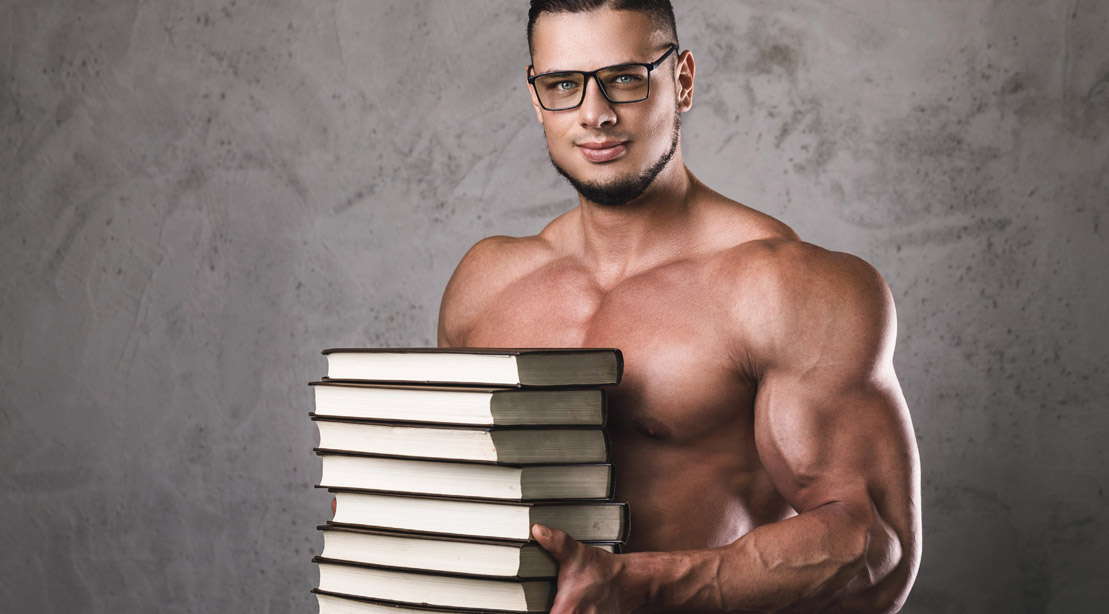 Muscular man wearing glasses and holding a stack of books for continuing education for fitness professionals