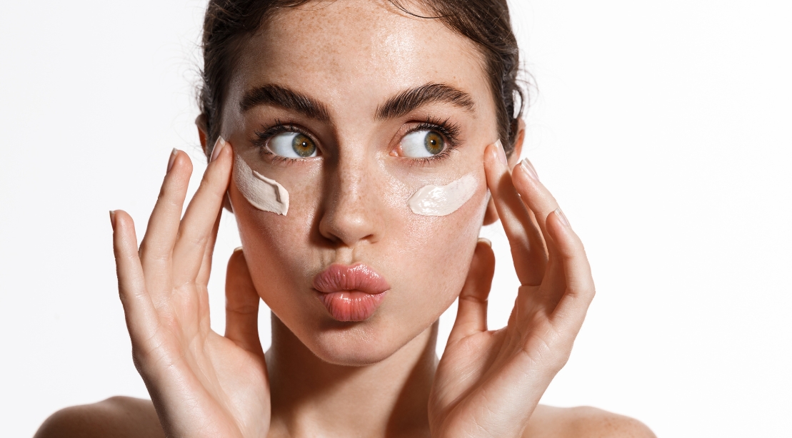 Close up beauty girl with freckles and thick eyebrows, applying moisturizing skincare cream