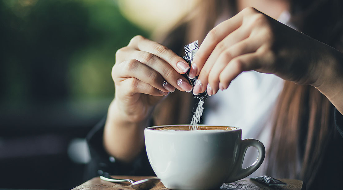 Woman pouring artificial sweeteners into her morning cup of coffee